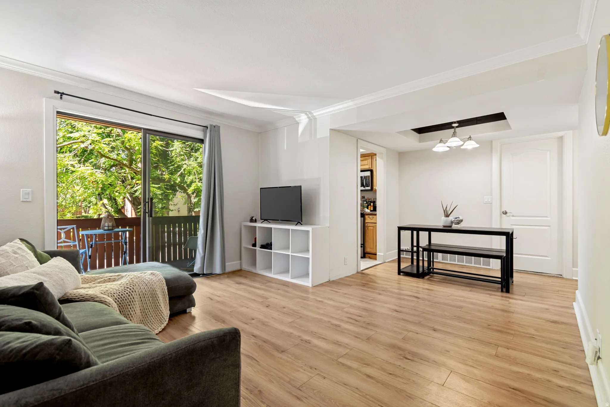 Open-concept living space featuring wood-finish flooring, a sliding glass door to a private balcony, crown molding, and a recessed ceiling fixture