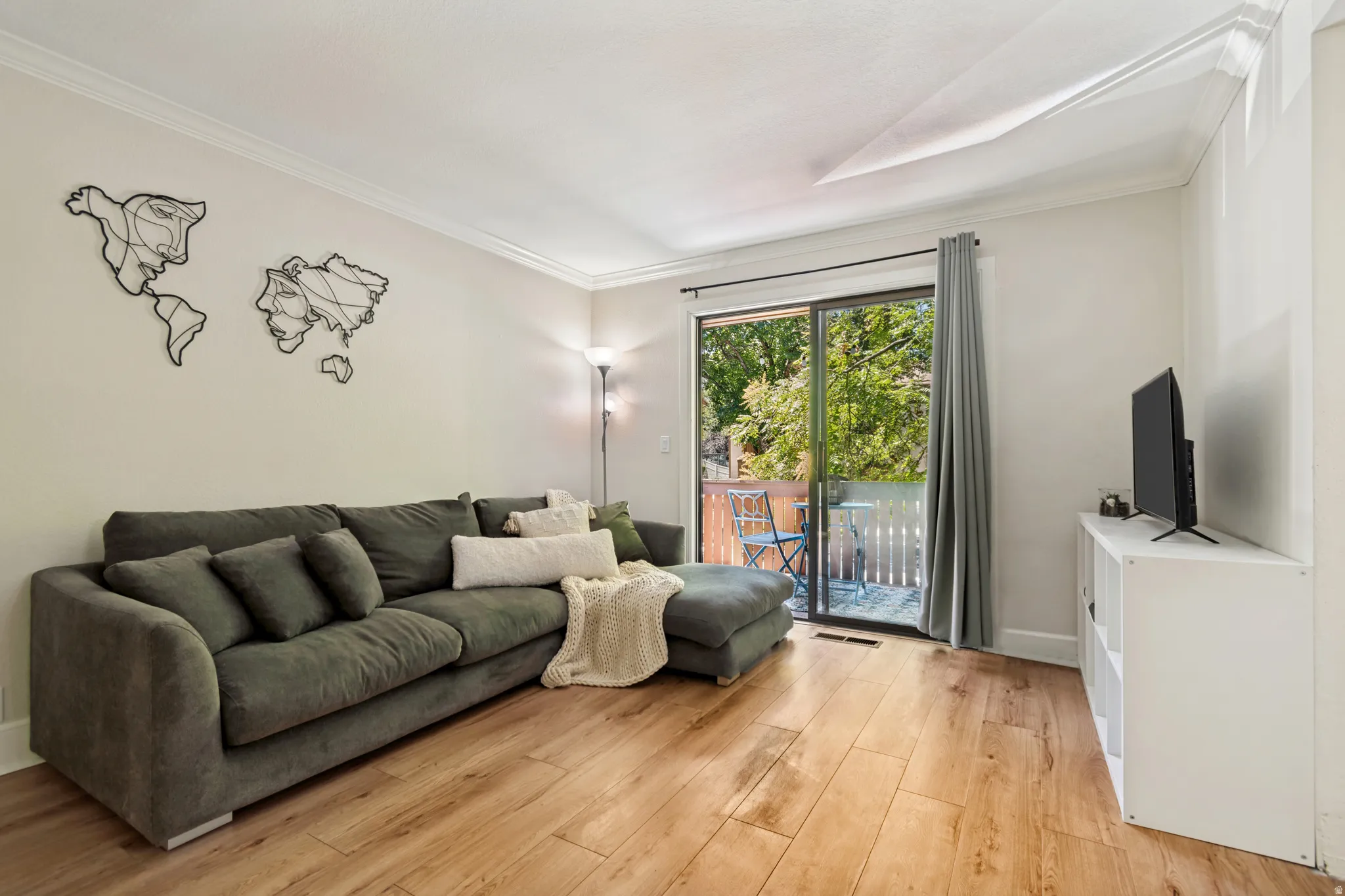 Living area featuring wood-finish flooring, crown molding, and a sliding glass door opening to an outdoor balcony with white railings
