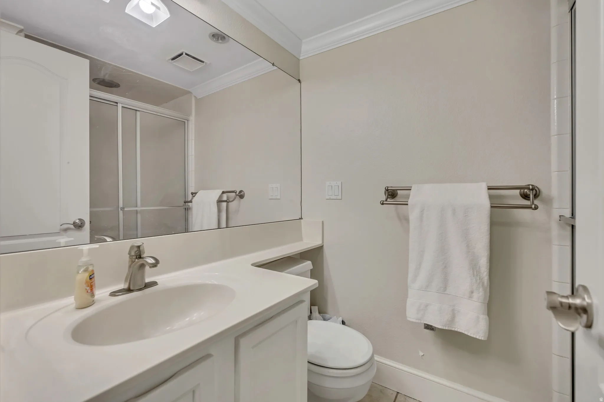 Bathroom featuring a single vanity with an integrated sink, brushed nickel faucet, large wall mirror, and a shower with sliding glass doors