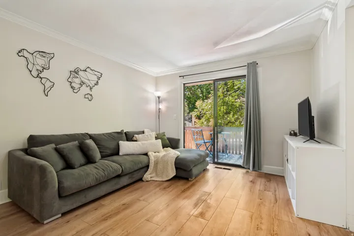 Living area featuring wood-finish flooring, crown molding, and a sliding glass door opening to an outdoor balcony with white railings