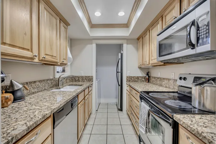 Galley kitchen featuring light wood cabinetry, granite countertops, tile flooring, a built-in microwave, and stainless steel appliances