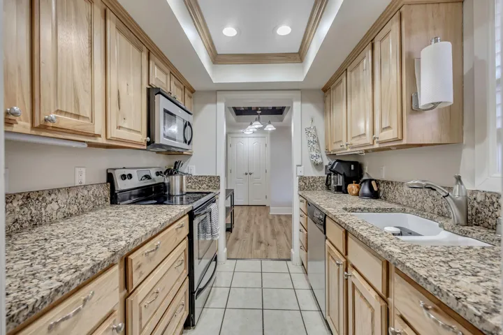 Galley kitchen featuring light wood cabinetry, stone countertops, a built-in microwave, an electric range, and a dual basin sink with a gooseneck faucet