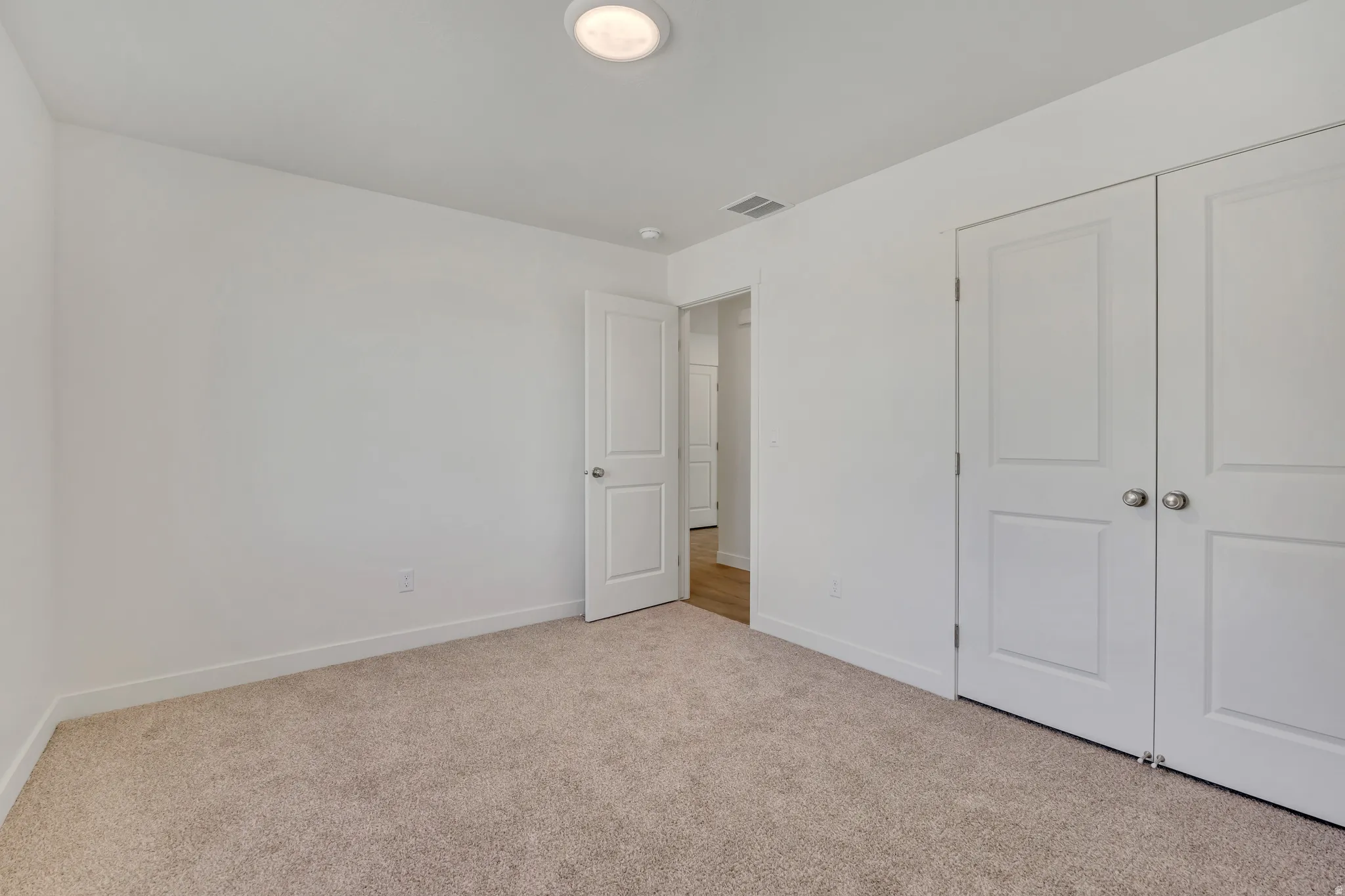 Carpeted room featuring white walls, a flush-mount ceiling light, white baseboards, and two white panel doors with brushed nickel hardware