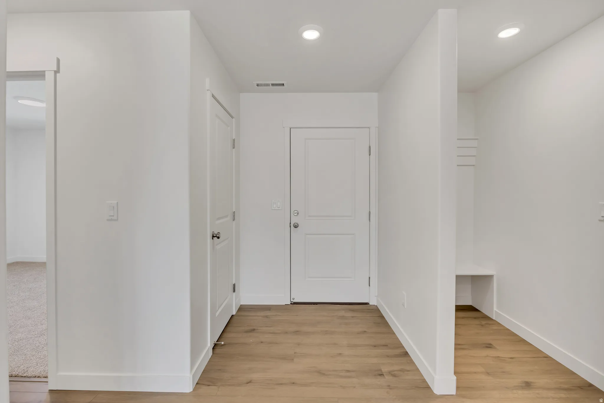 Entryway featuring wood-finish flooring, recessed lighting, white panel doors, and a built-in bench with coat hooks