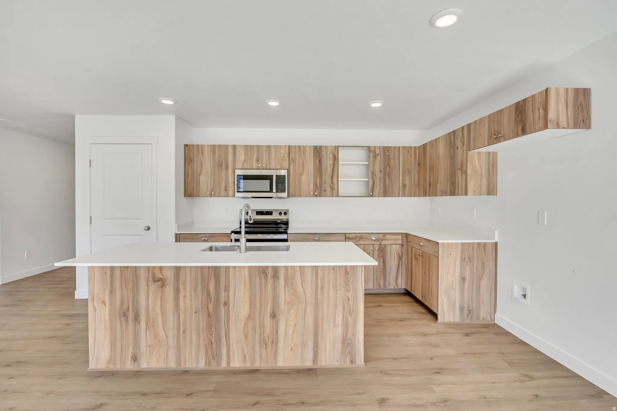 Kitchen featuring a large central island, coordinating wood-finish cabinetry, white countertops, and stainless steel appliances including a microwave and range