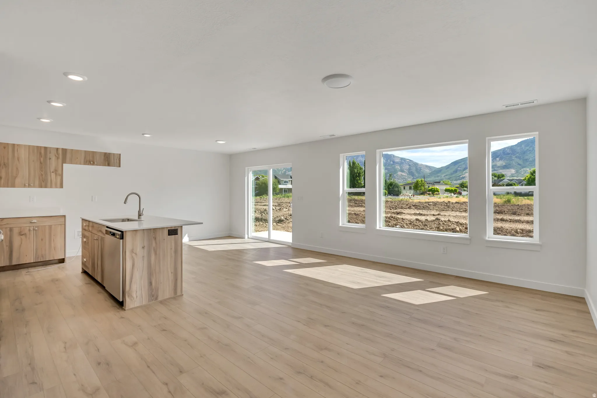 Open-concept living space featuring wood-finish flooring, recessed lighting, and a kitchen island with integrated sink and dishwasher