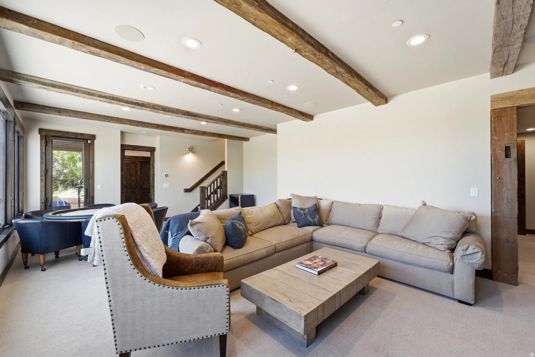 Spacious living area featuring exposed wood beams, recessed lighting, carpeted flooring, and a large window