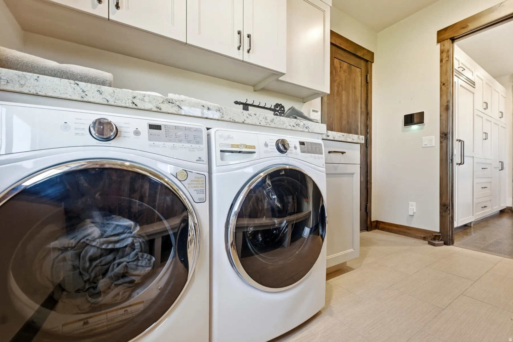 Dedicated laundry area featuring a granite-style countertop, white cabinetry with dark hardware, light-toned flooring, and a natural wood-trimmed doorway