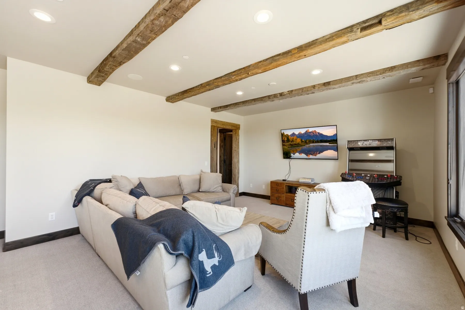 Living area featuring exposed wood beams, recessed lighting, carpet flooring, a wood-finish entertainment console, and a large window with dark trim