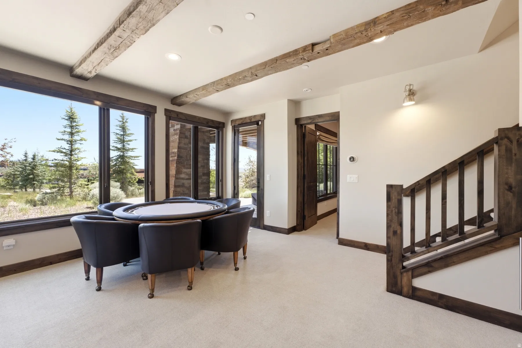 Spacious room featuring exposed wood beams, light-colored carpeting, and extensive window-walls providing abundant natural light