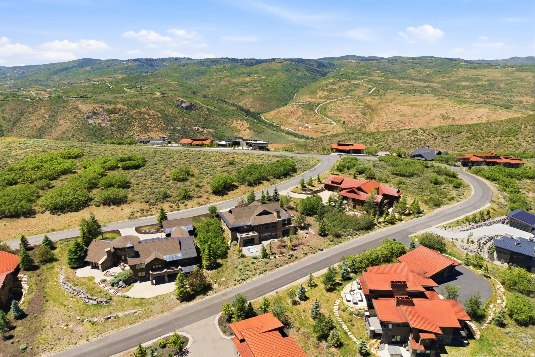 Expansive mountain landscape with winding roads and scattered residential properties, featuring varied architectural styles and pitched roofs