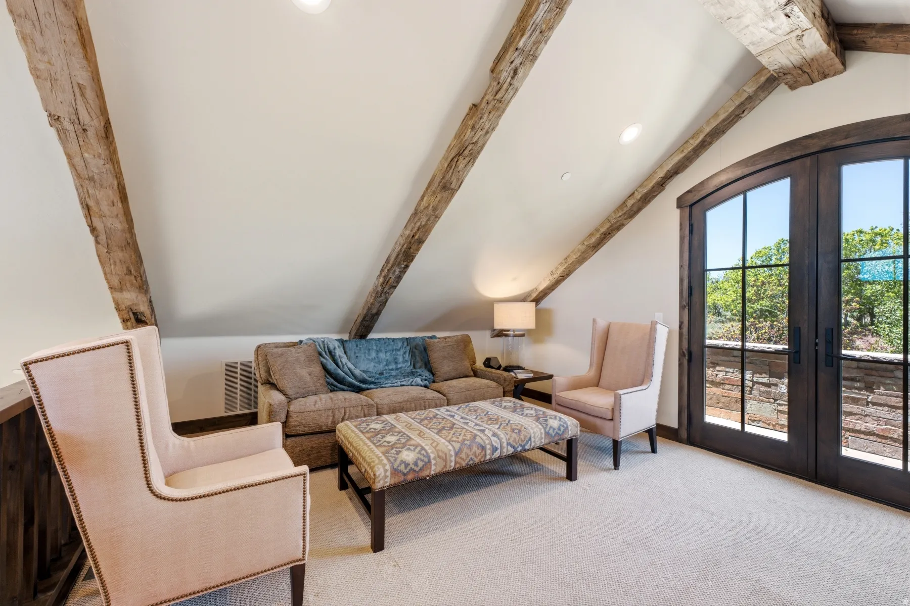 Vaulted ceiling featuring exposed wood beams, recessed lighting, arched French doors with dark wood frames, and light-toned carpeting