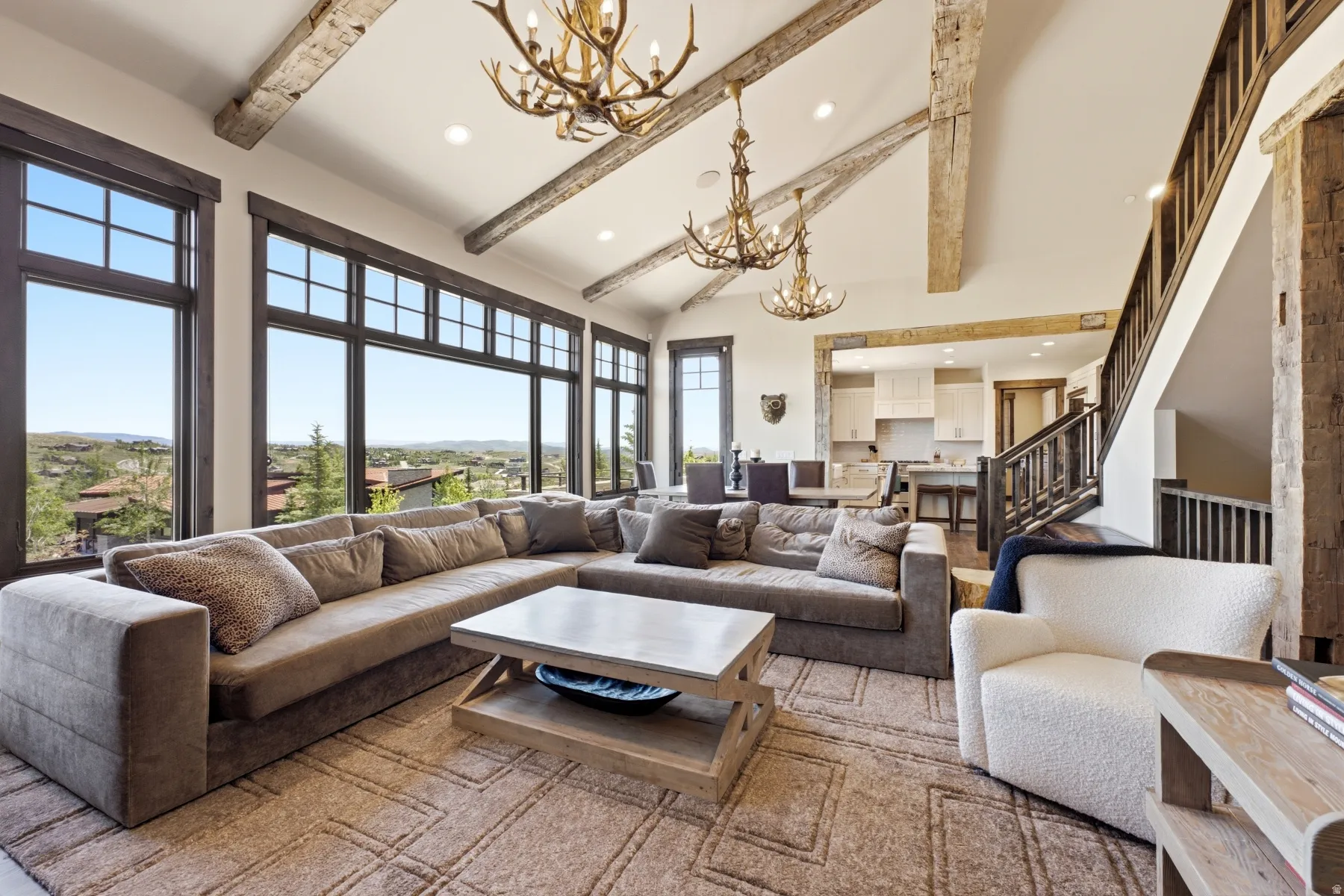 Great room featuring vaulted ceilings with exposed wood beams, expansive windows, multiple antler chandeliers, and wood-finish flooring