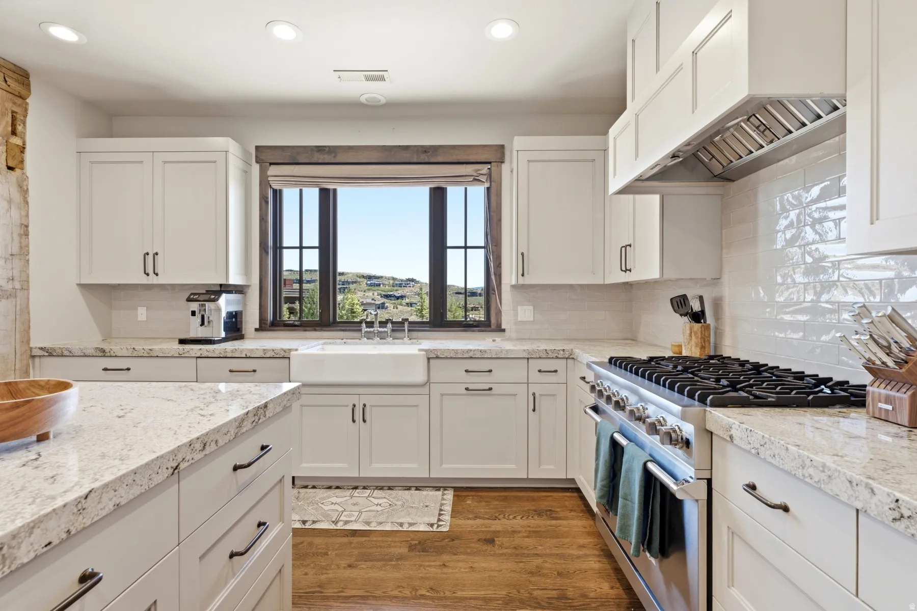 Gourmet kitchen featuring white shaker cabinetry, speckled countertops, a farm sink, stainless steel range with a professional hood, and wood-finish flooring