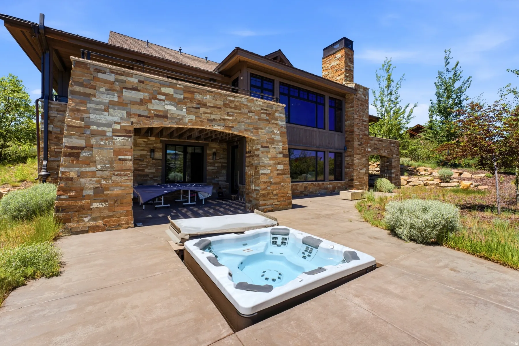 Outdoor patio featuring an embedded hot tub, stone-clad exterior, and a covered patio area with a dark wood ceiling