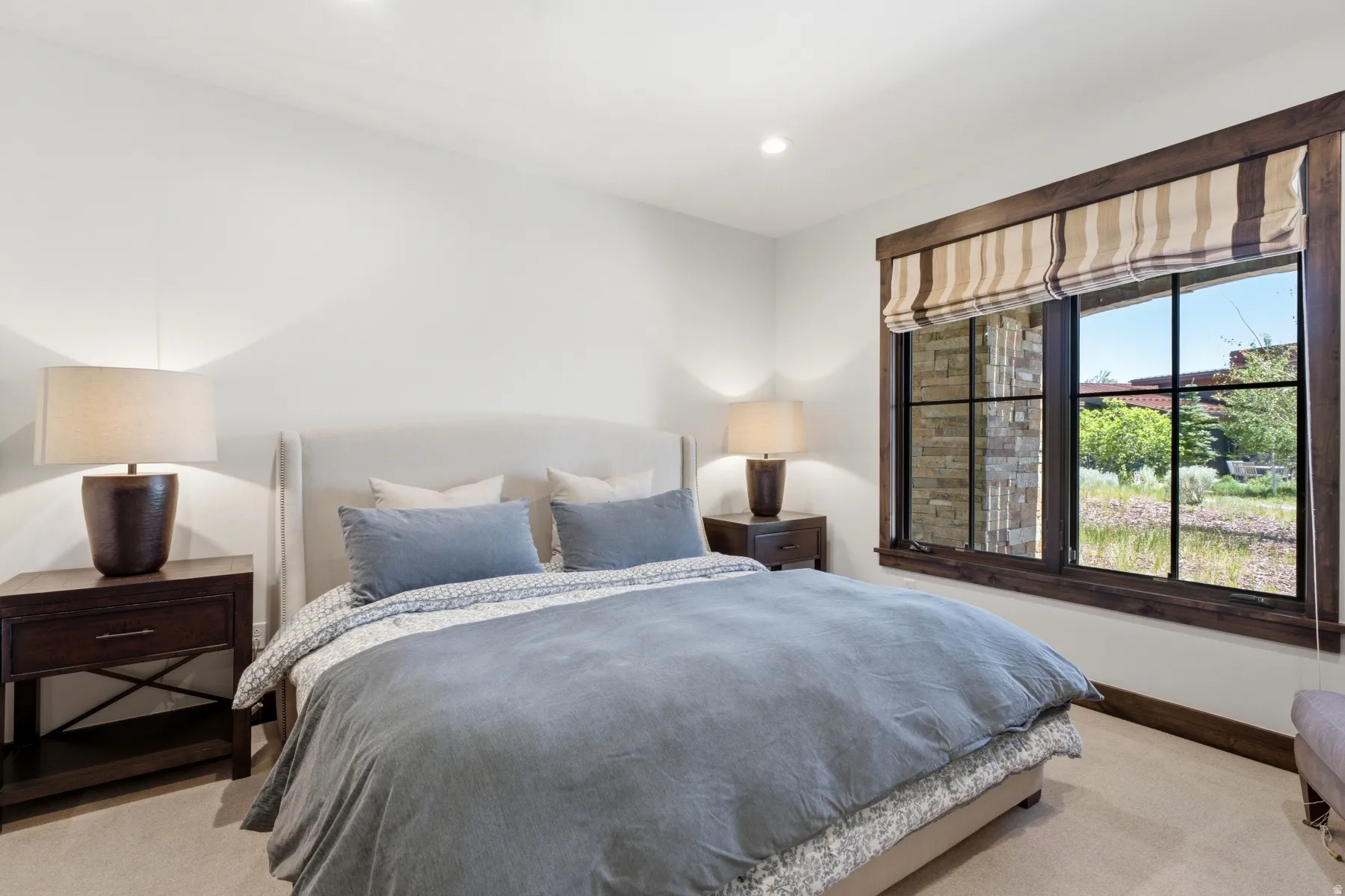 Bedroom featuring a large window with dark wood trim, offering exterior landscaping views