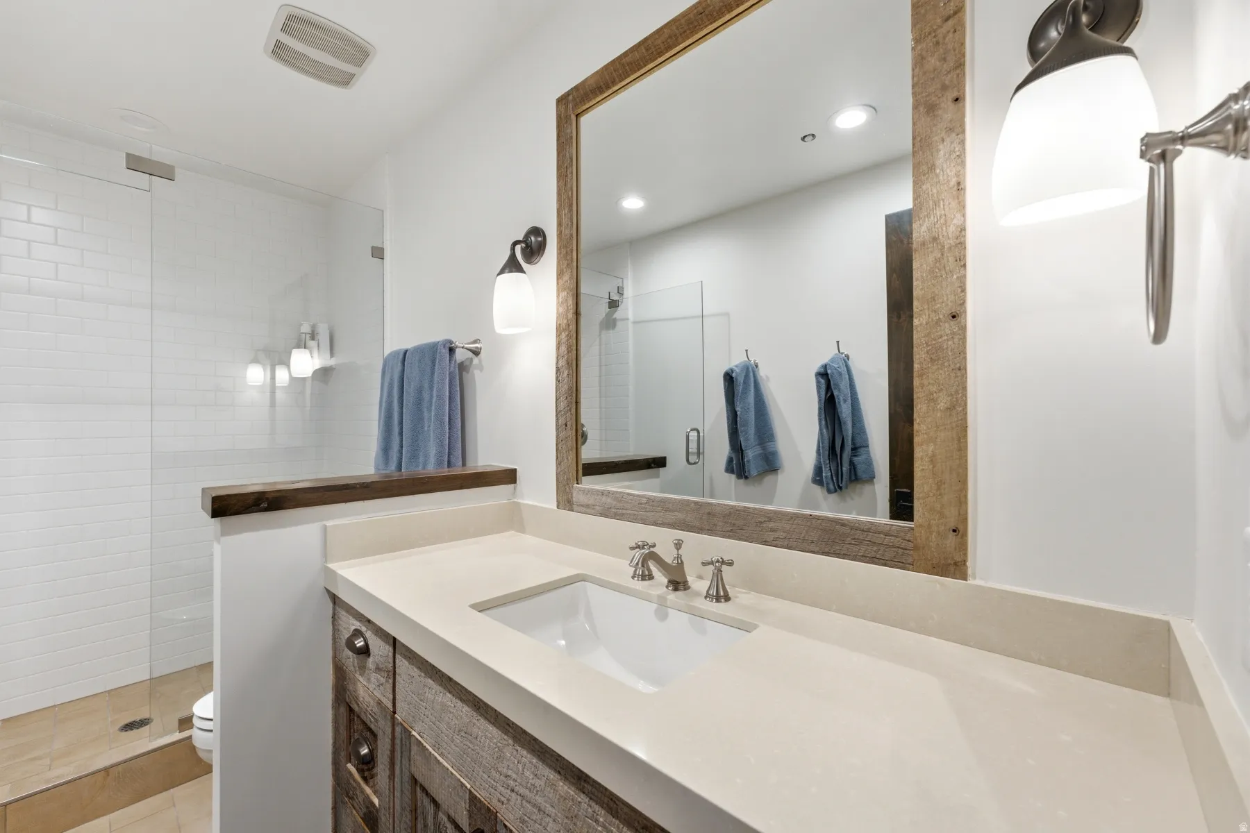Bathroom vanity featuring a light-toned countertop, under-mount sink, and wood-finish cabinetry