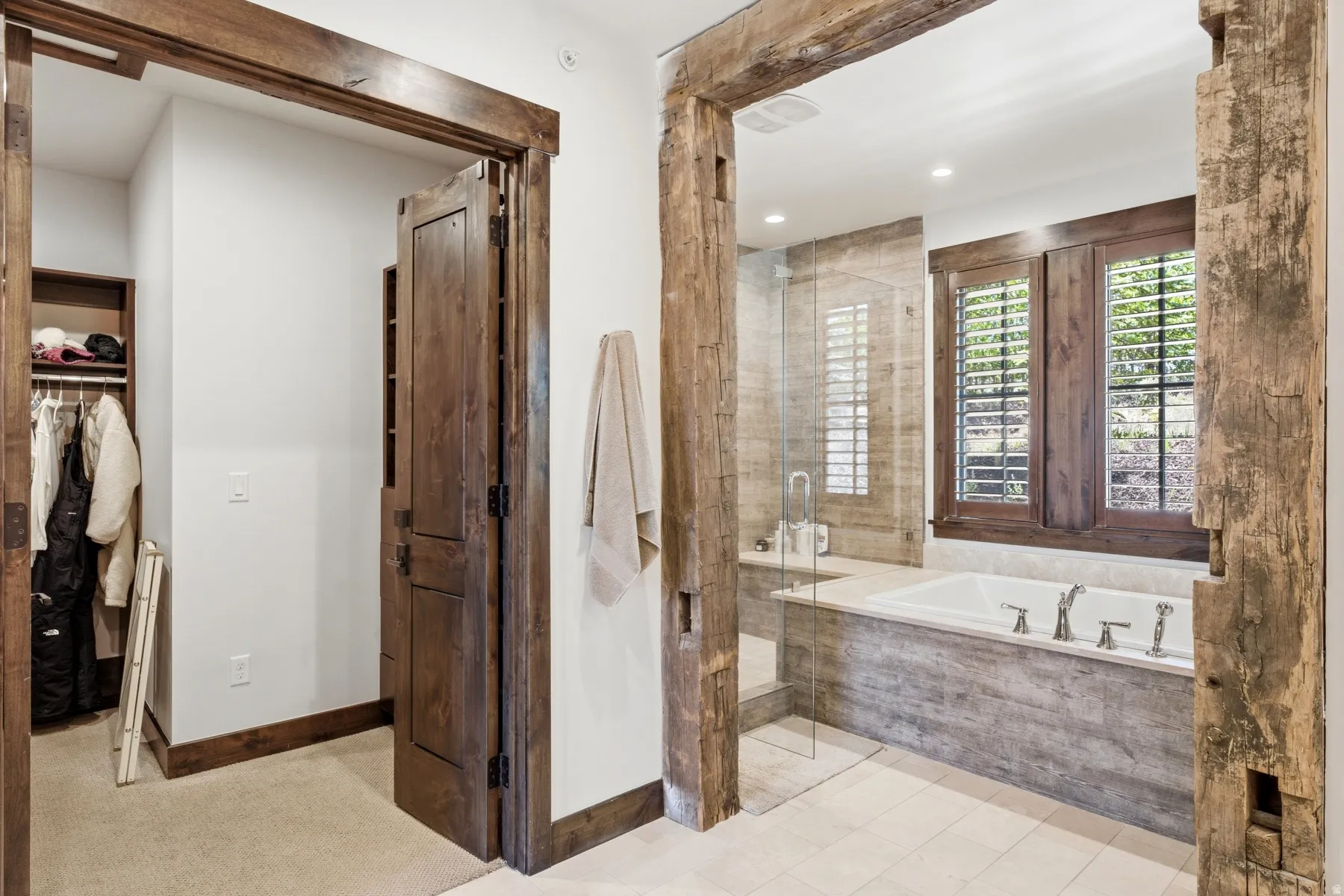 Bathroom featuring a built-in soaking tub with a tiled surround, a glass-enclosed shower, and wood-framed windows with louvered shutters