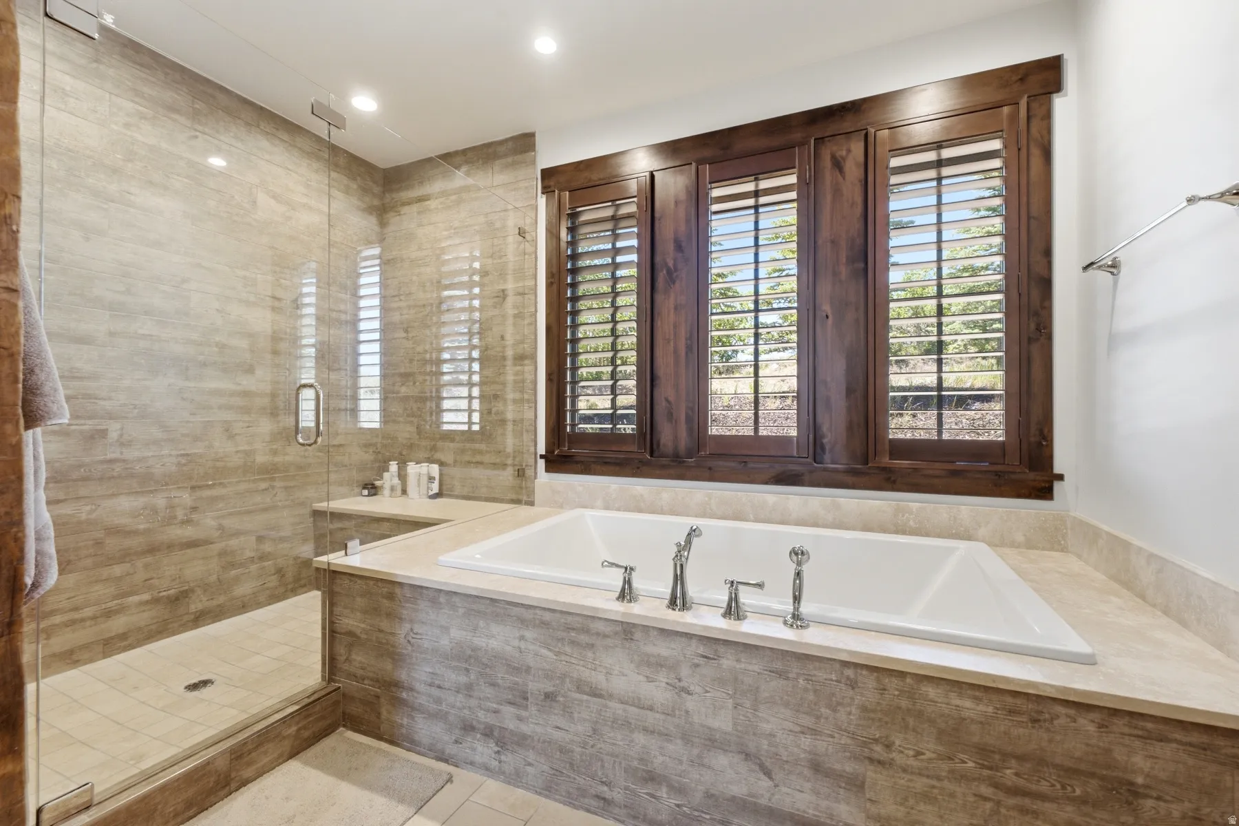 Built-in soaking tub with polished chrome fixtures, surrounded by a stone-finish tile deck and wall