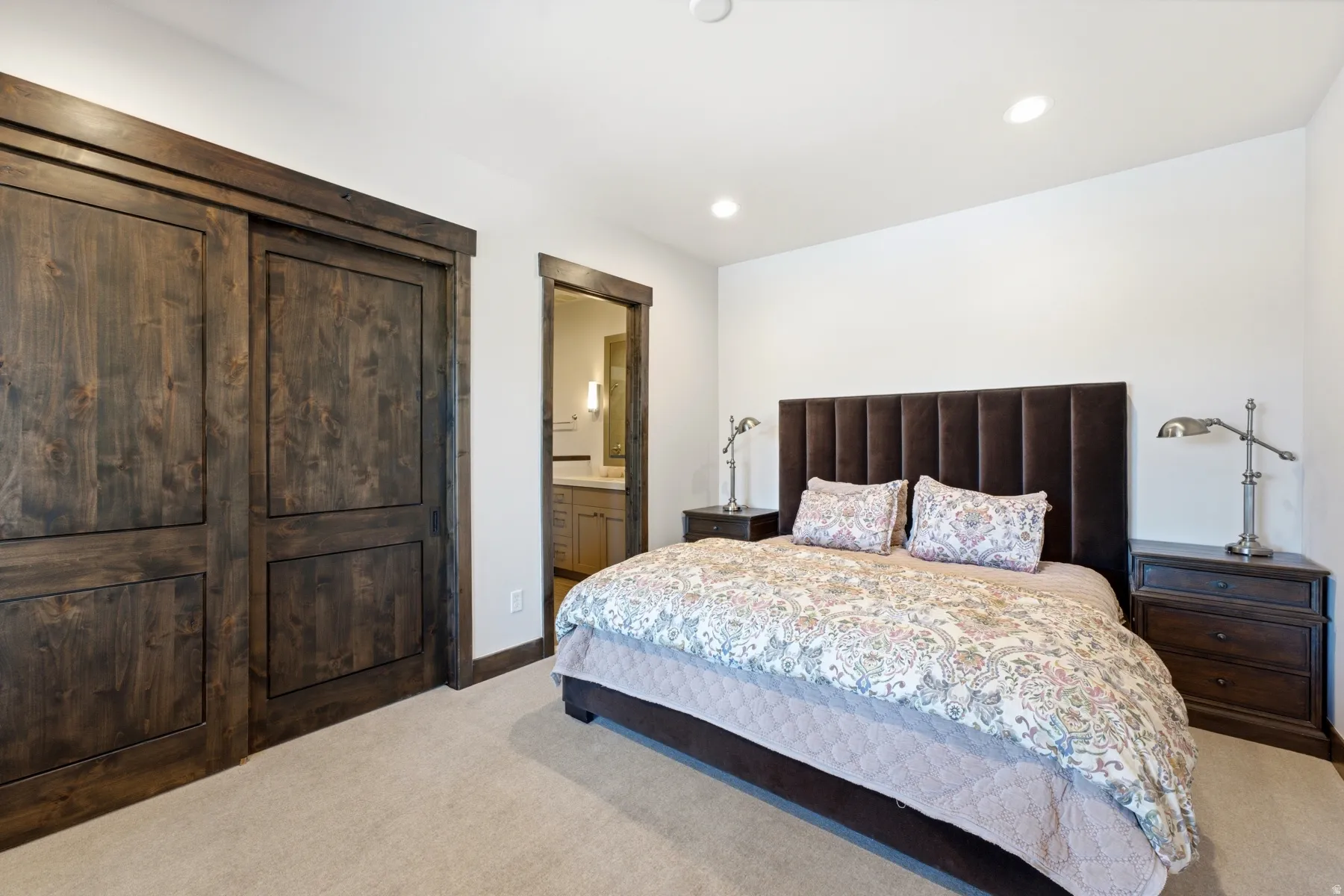 Recessed lighting illuminates a space featuring light carpet flooring and white walls