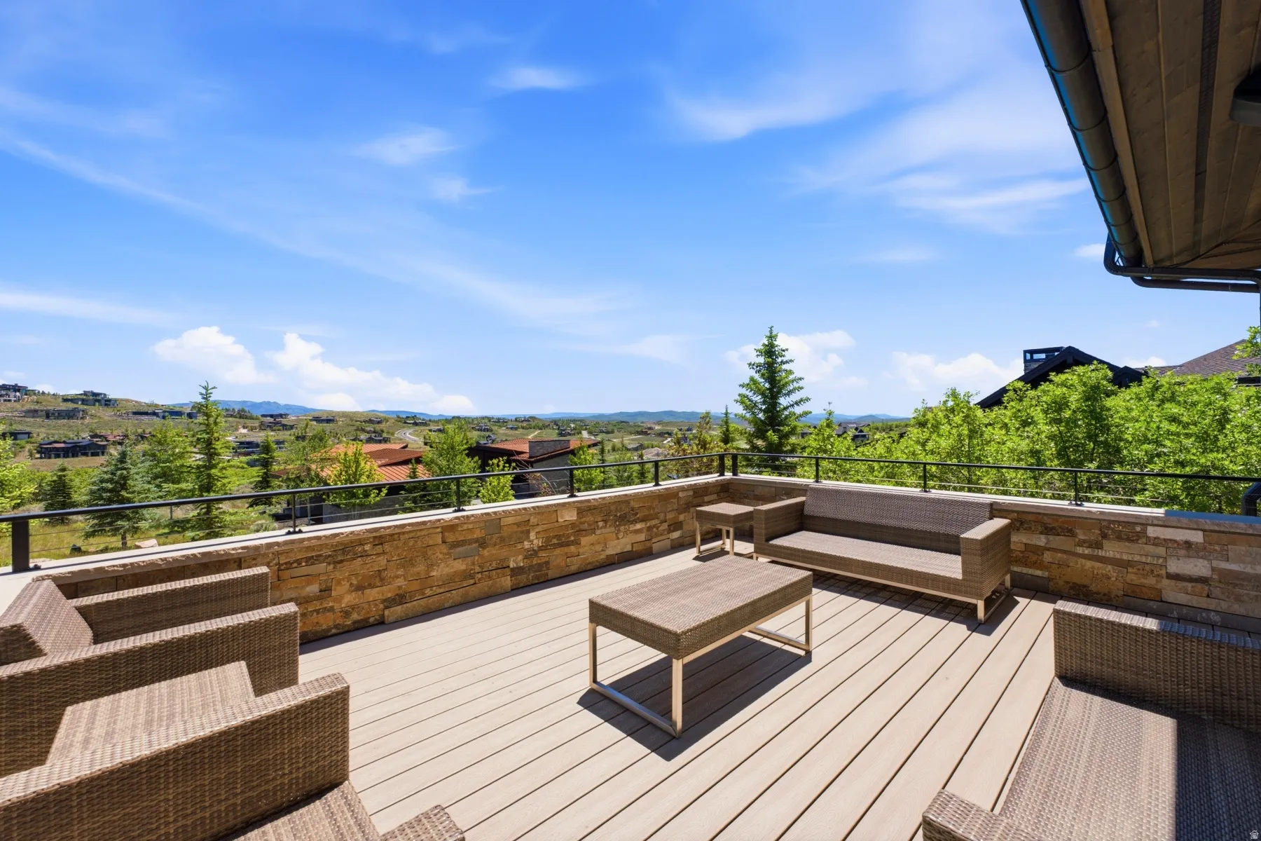 Expansive exterior deck featuring composite decking, a stone accent wall, and a black metal railing