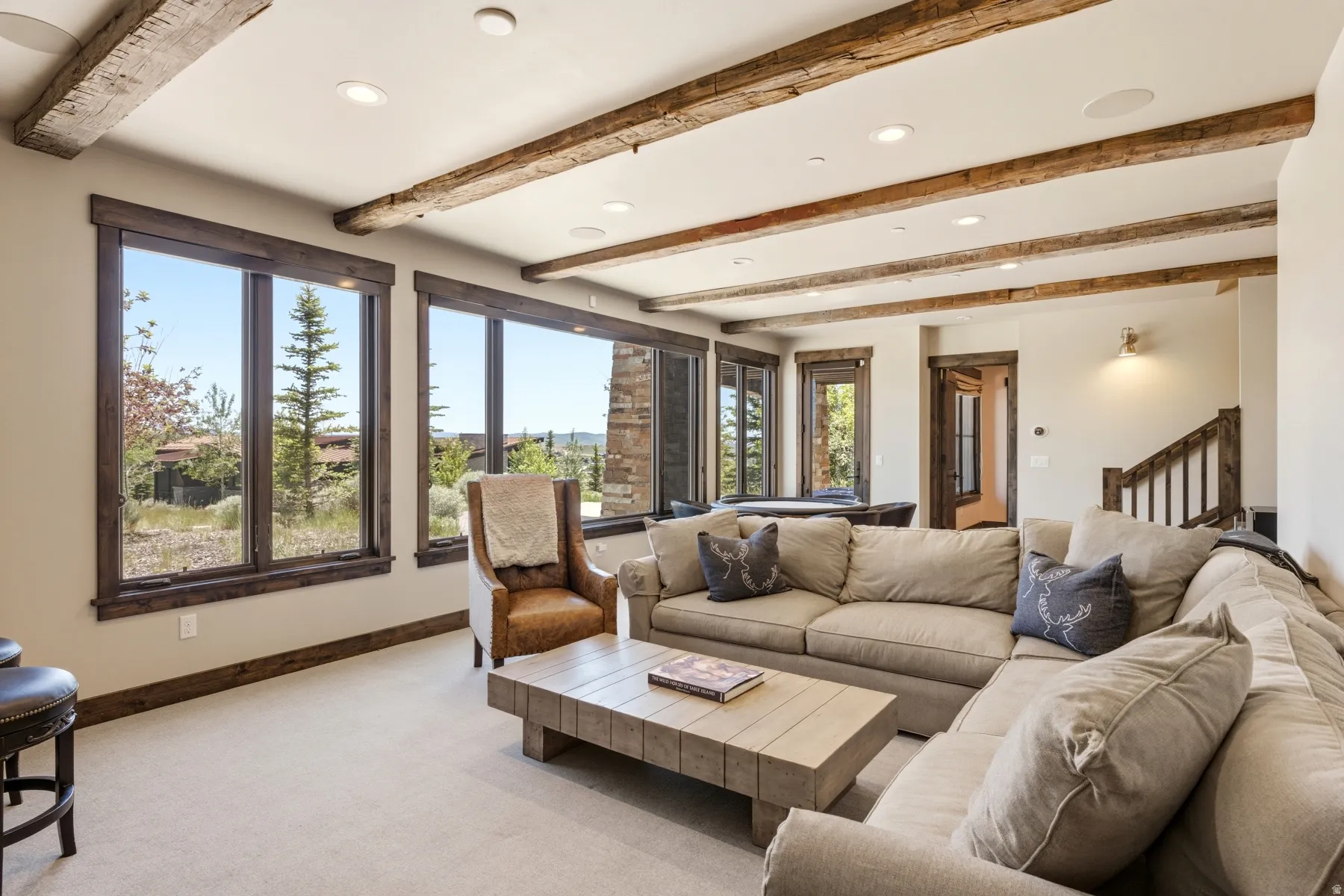 Spacious living area featuring exposed wood ceiling beams, recessed lighting, and large windows with wood-finish trim