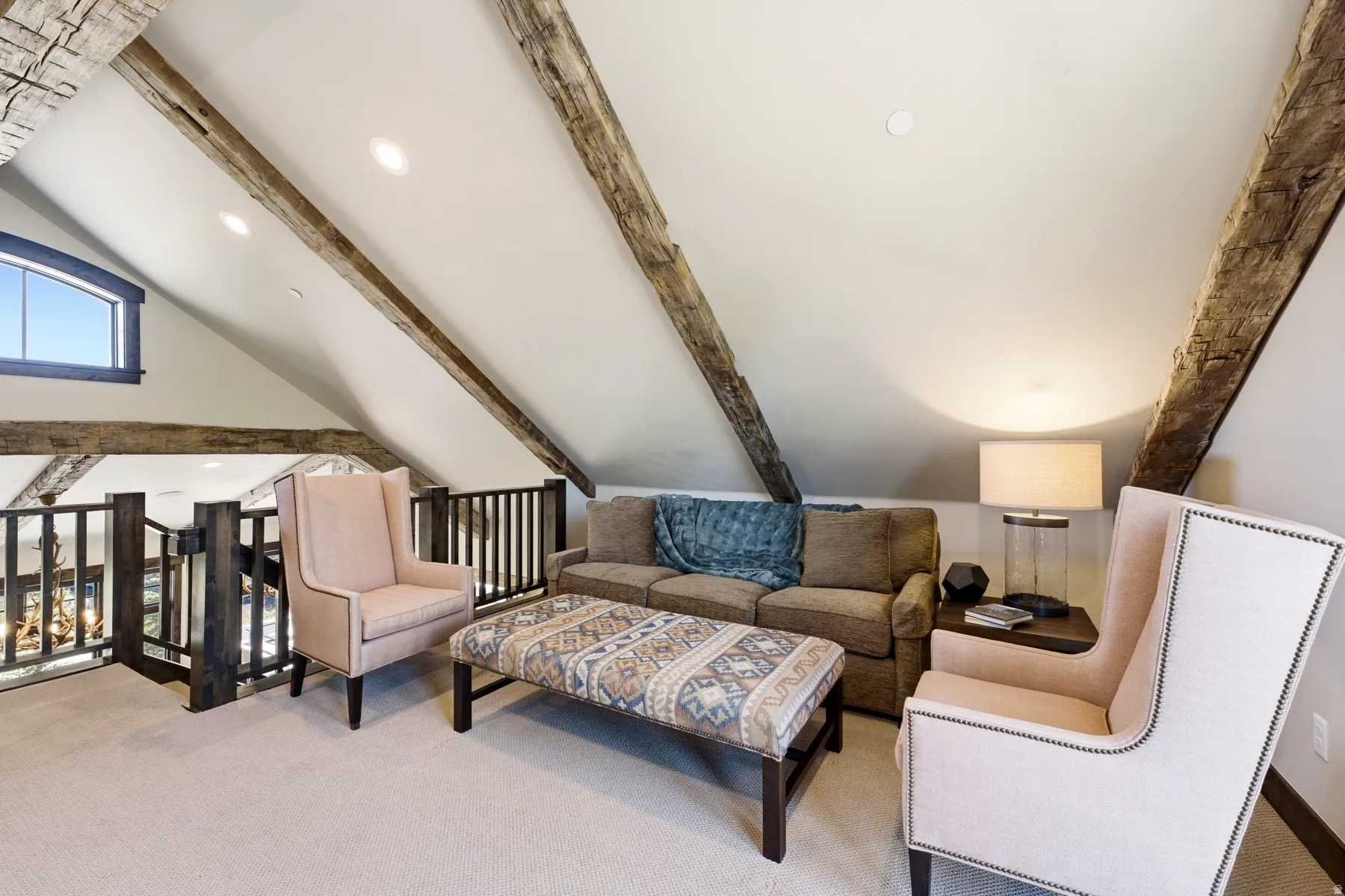 Loft area featuring exposed wood beams, vaulted ceilings, recessed lighting, a triangular window, and dark wood railings