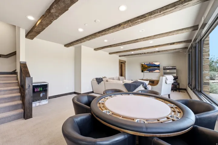 Carpeted lower-level room featuring exposed wood ceiling beams, recessed lighting, and a beverage cooler