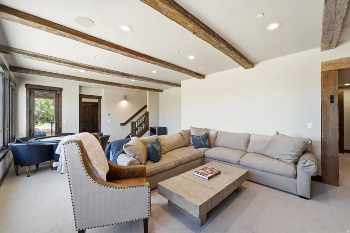 Spacious living area featuring exposed wood beams, recessed lighting, carpeted flooring, and a large window