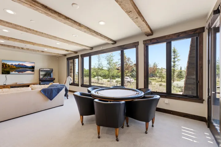 Spacious interior featuring exposed wood ceiling beams, recessed lighting, a wall of large windows with dark wood trim, and light-colored carpeting