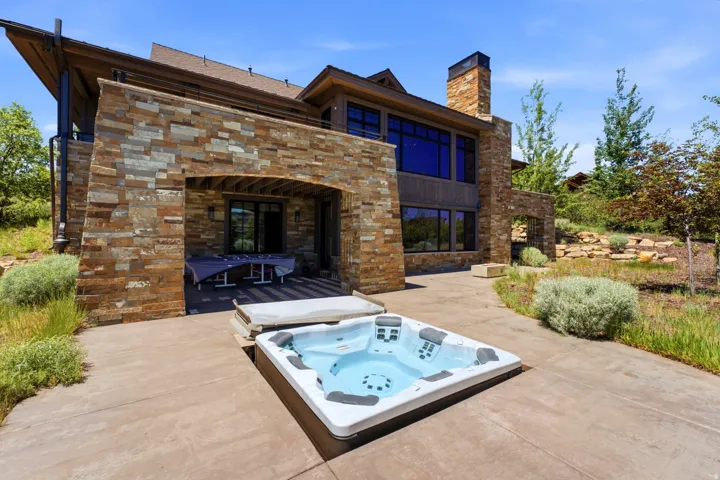 Outdoor patio featuring an embedded hot tub, stone-clad exterior, and a covered patio area with a dark wood ceiling