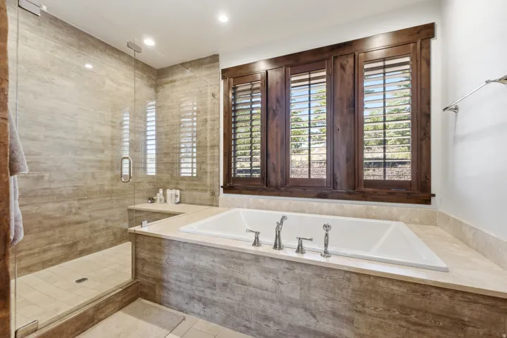 Built-in soaking tub with polished chrome fixtures, surrounded by a stone-finish tile deck and wall