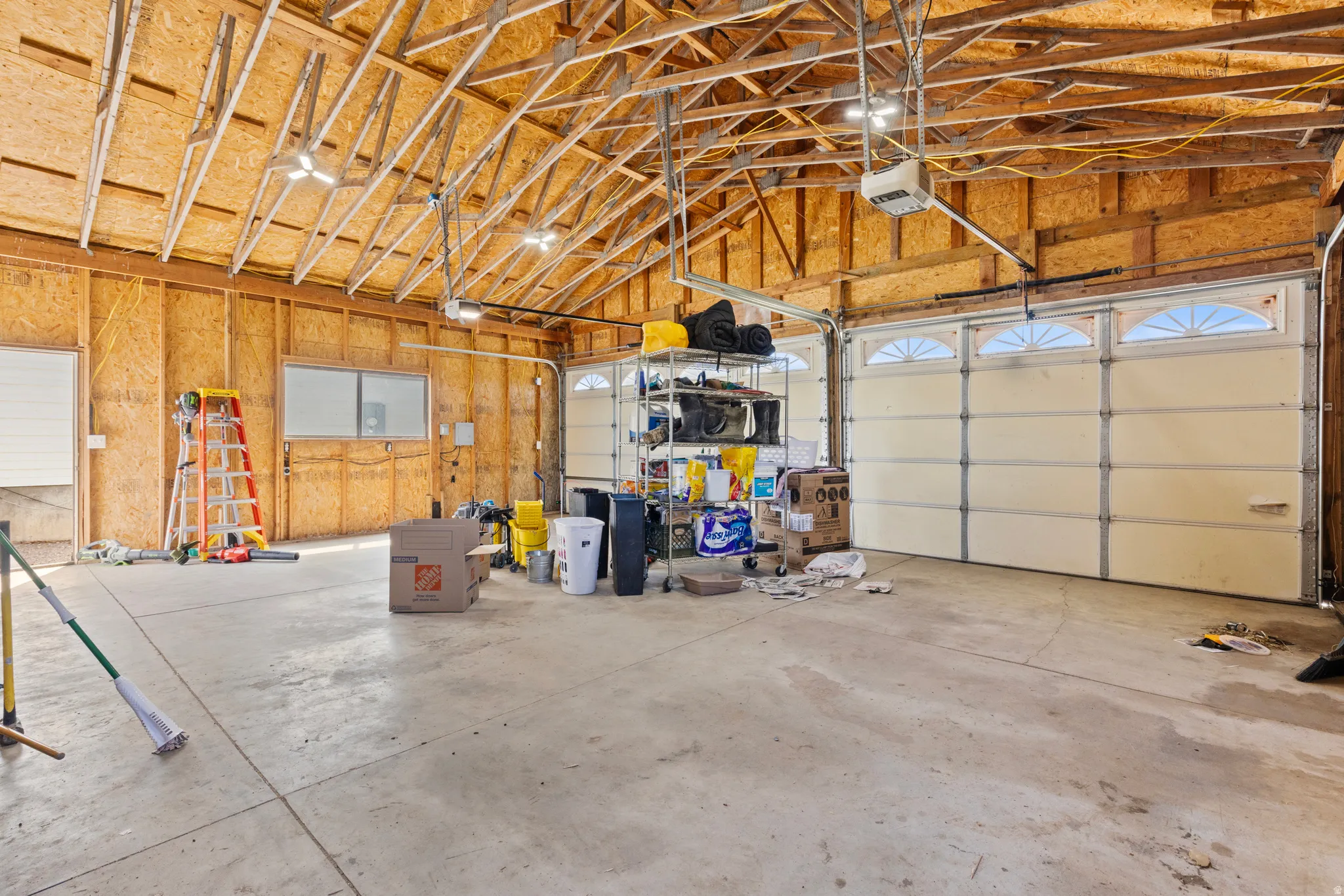 Spacious garage featuring exposed wood trusses, concrete flooring, overhead lighting, and two garage doors with arched window panels