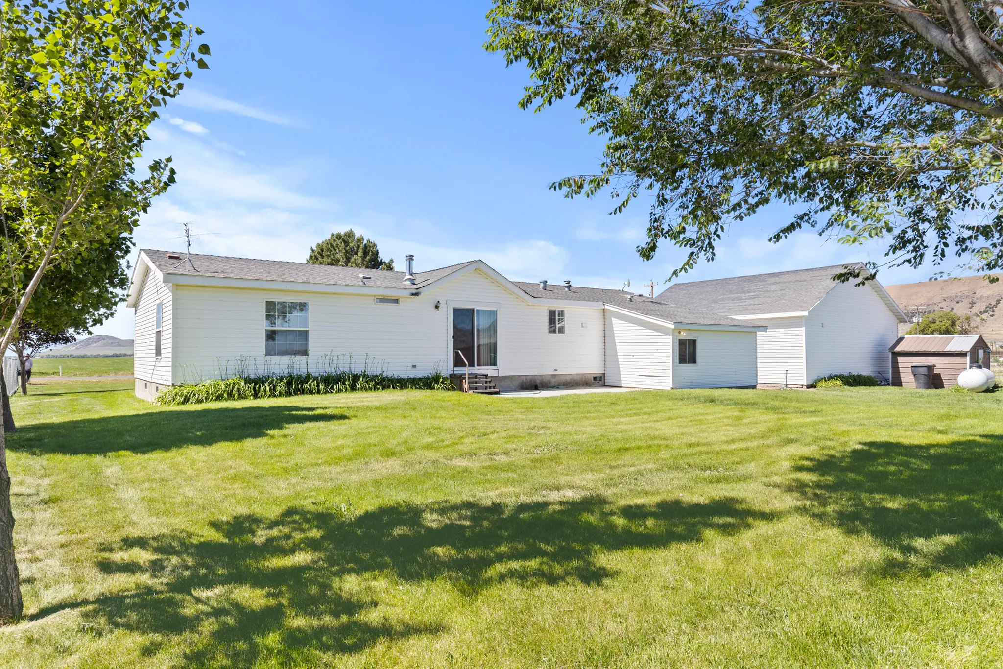 Expansive green lawn bordering the white siding residence with a sliding glass door and an additional structure