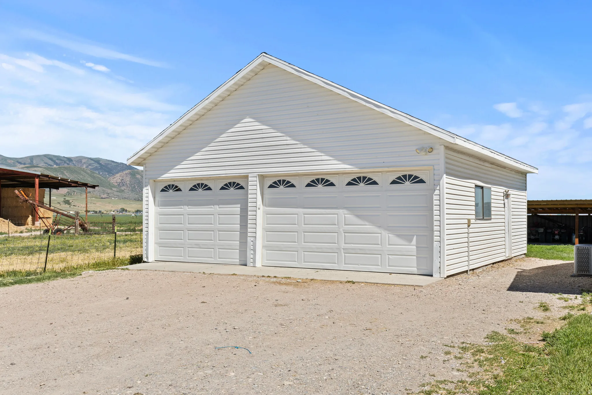 Detached two-car garage with white vinyl siding, decorative arched windows on garage doors, a side access door, and a single side window, all set on a gravel surface