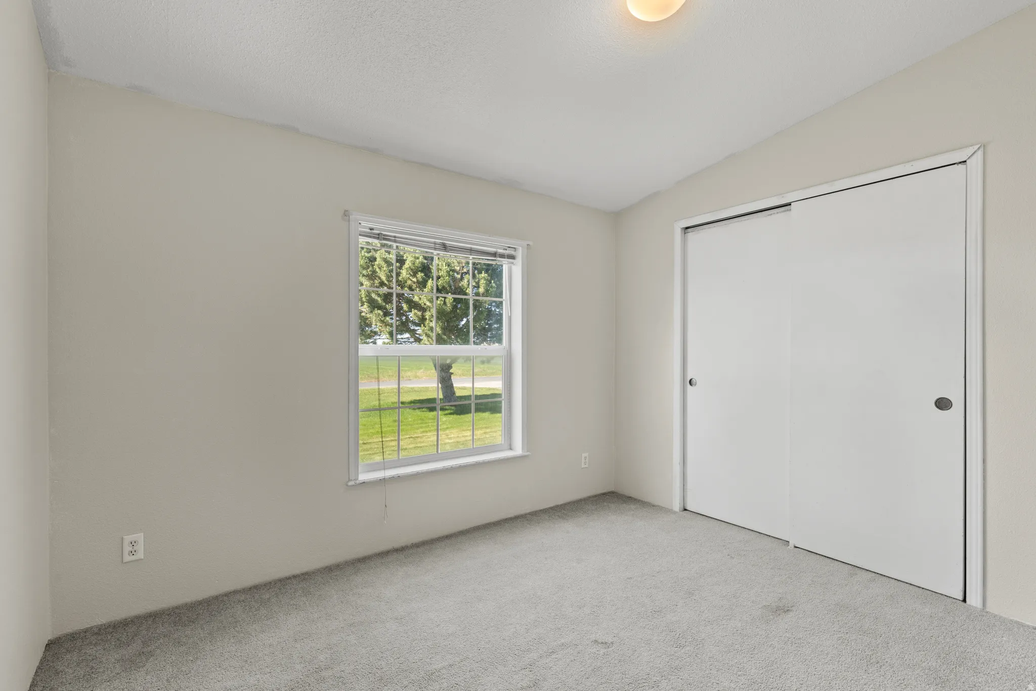 Room featuring light gray walls, gray carpet flooring, a white-framed window, and a built-in sliding door closet