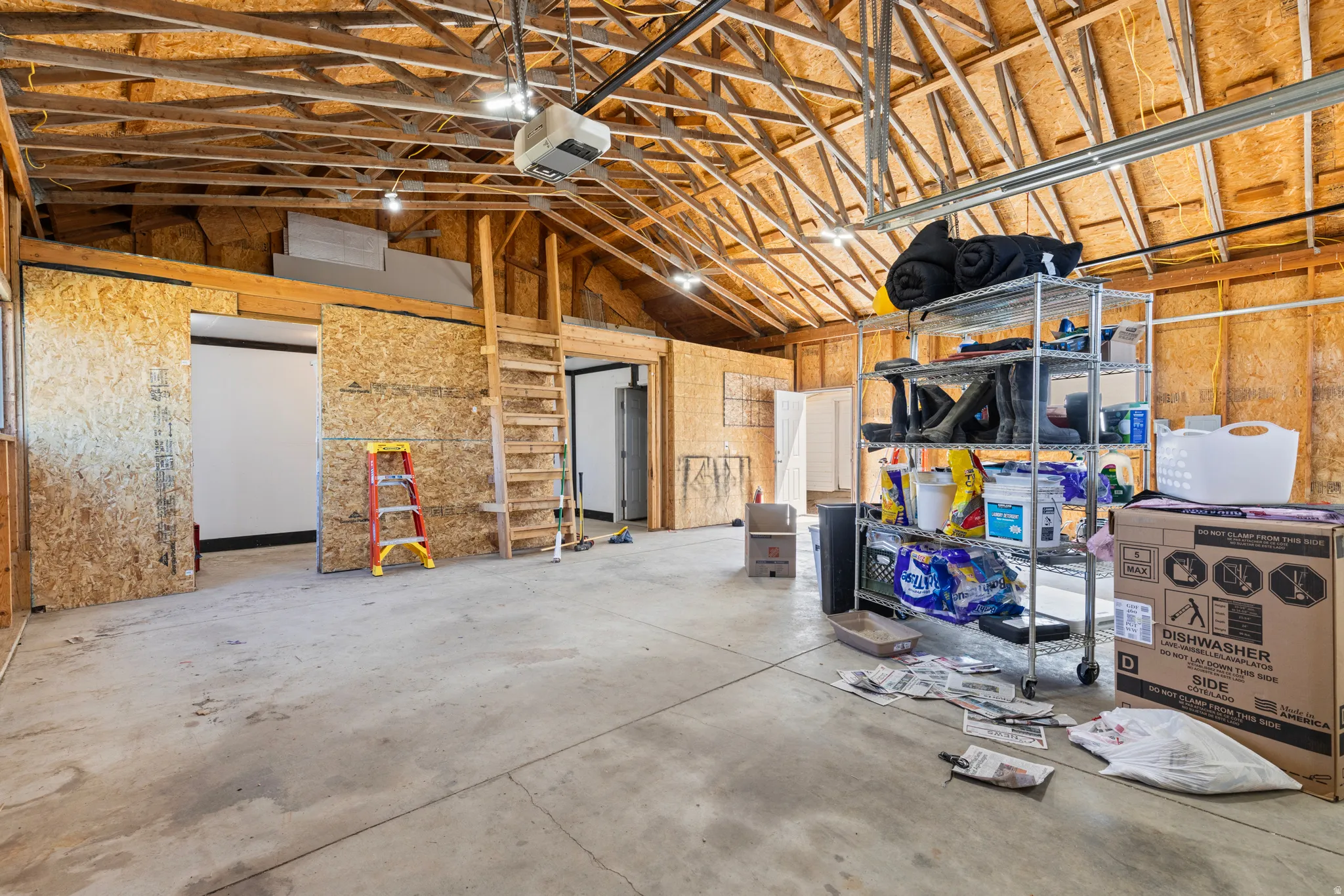 Spacious garage with exposed wood trusses, concrete flooring, track lighting, and a built-in ladder providing access to an upper level