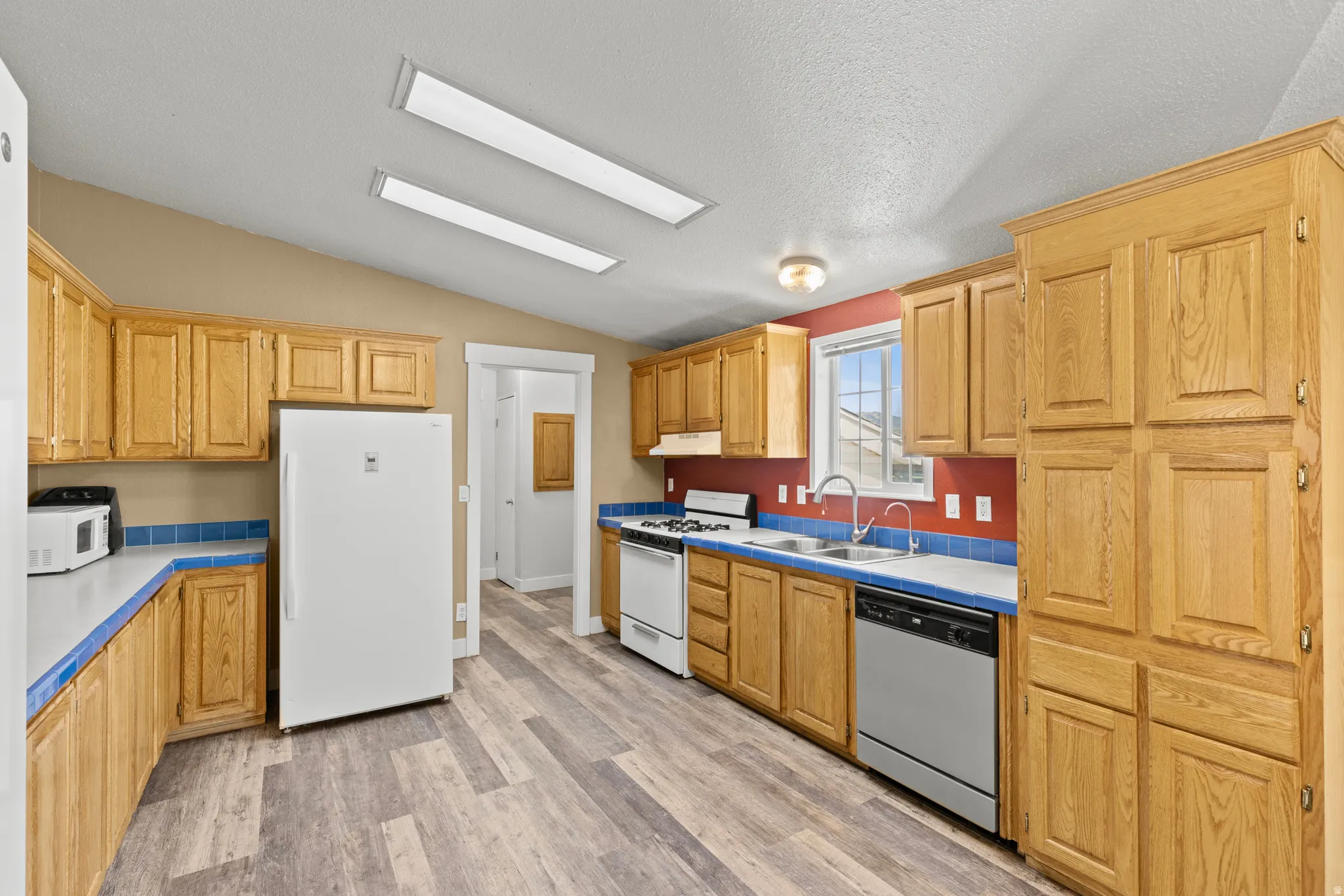 Spacious kitchen featuring wood-finish flooring, light wood cabinetry, white appliances, and a double basin sink