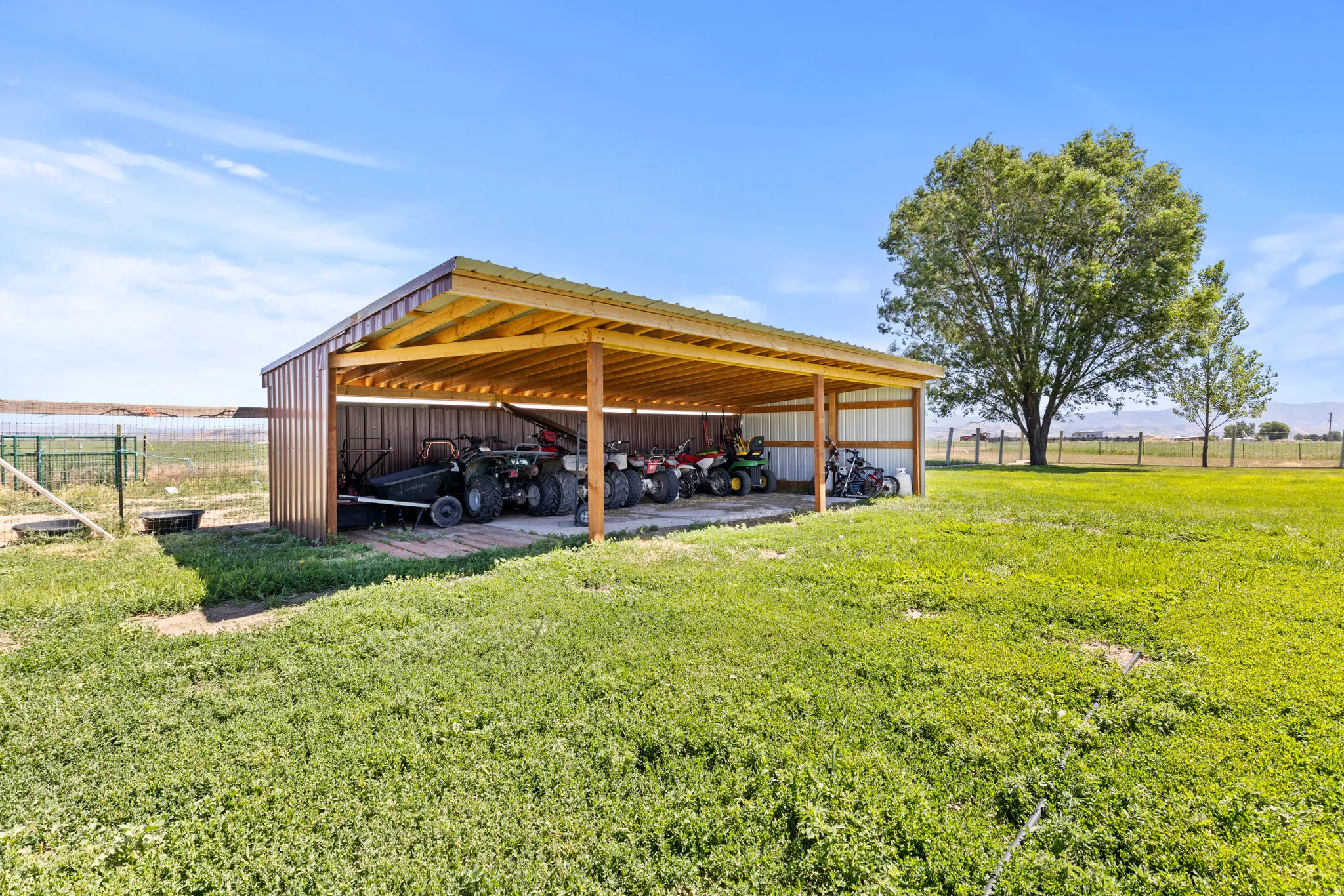 Open-sided shed with a brown metal roof and siding, supported by wood posts, offering extensive covered storage