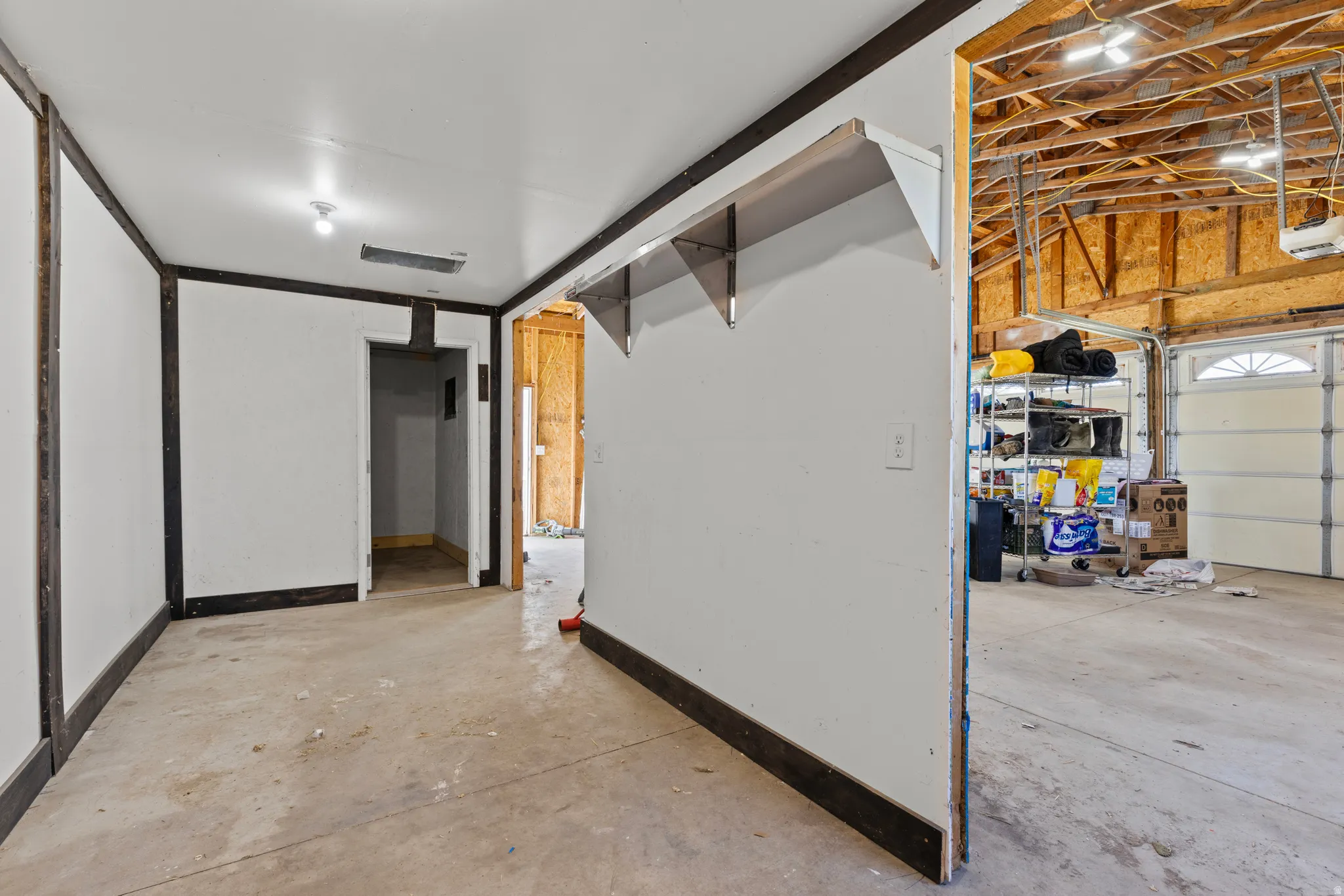 Unfinished interior space featuring a concrete floor, white walls with dark trim, and exposed ceiling beams