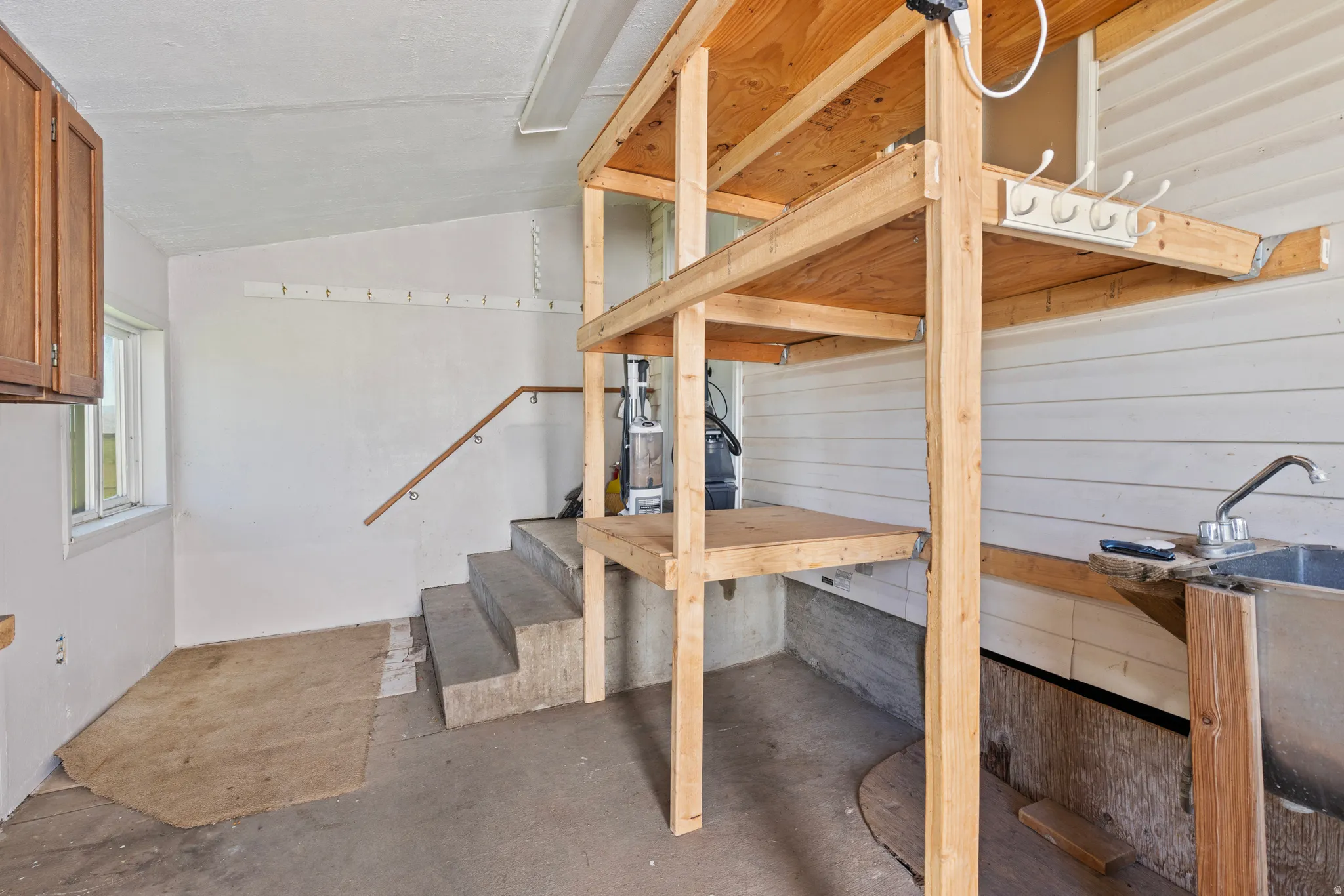 Utility area featuring an integrated sink, built-in wooden shelving, concrete steps with a handrail, and wall-mounted storage hooks