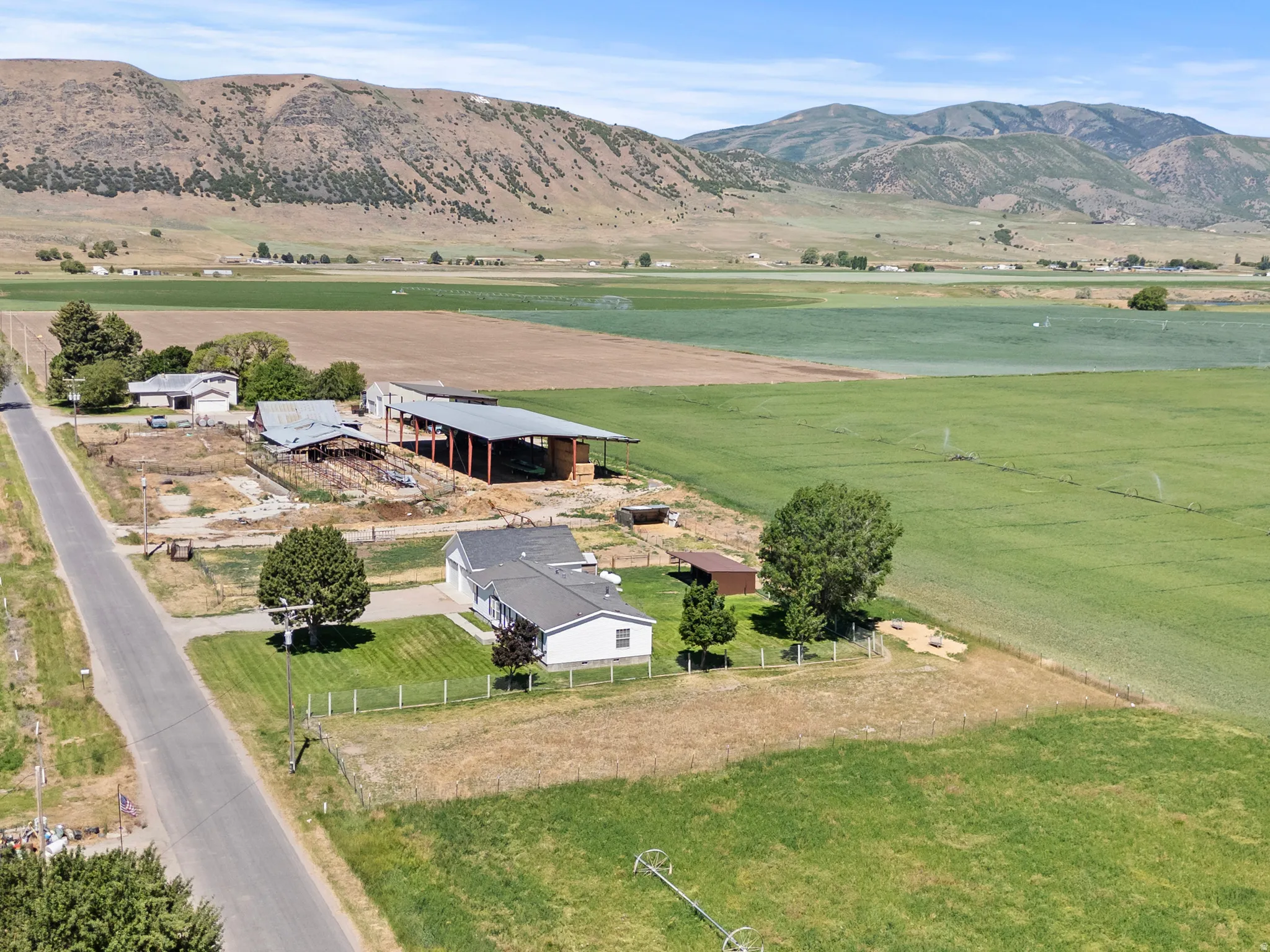 Aerial perspective showcasing an expansive agricultural property with a single-story residence, multiple outbuildings, and cultivated fields