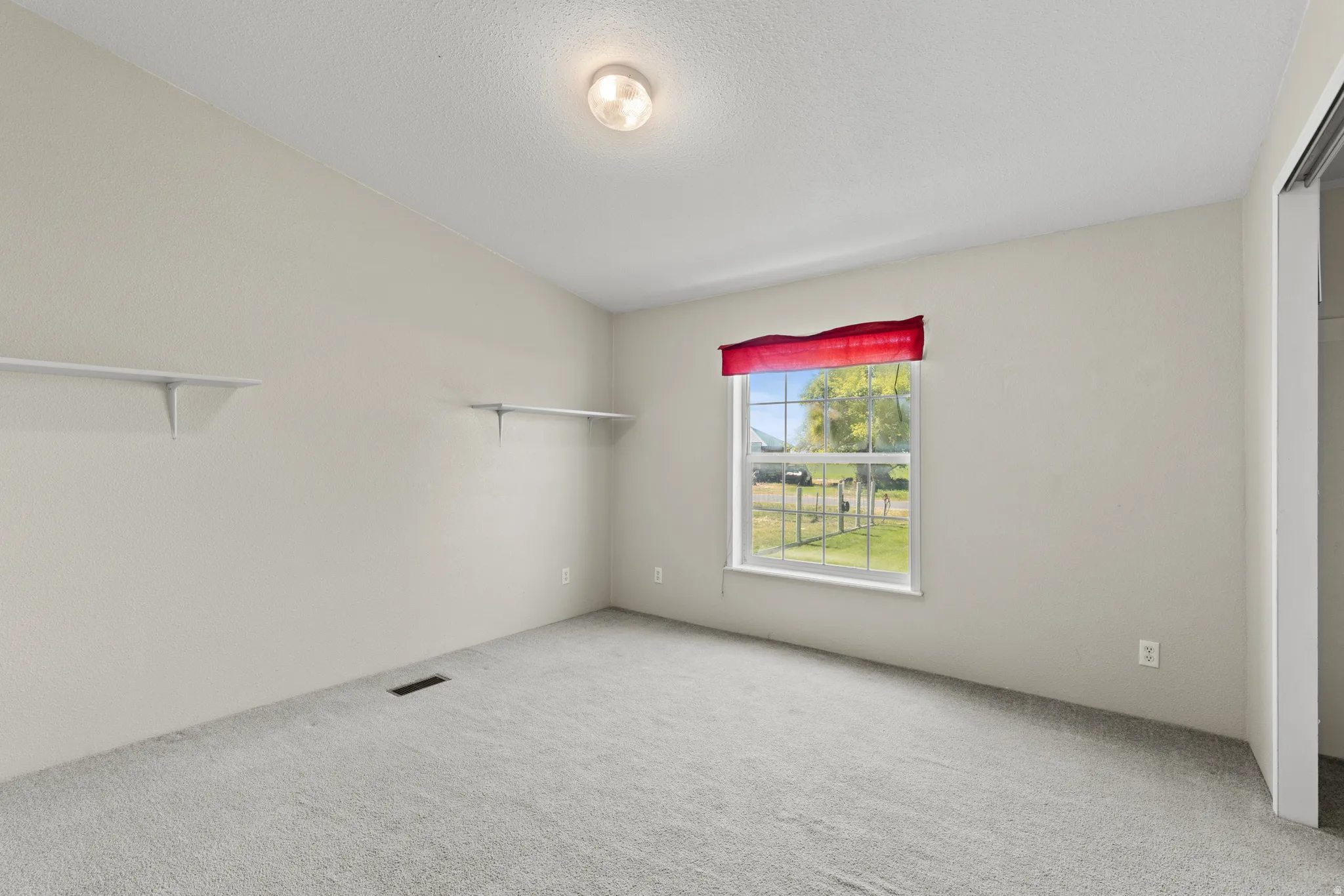 Carpeted room featuring a single window with exterior views, light-toned wall paint, and a built-in closet with bifold doors