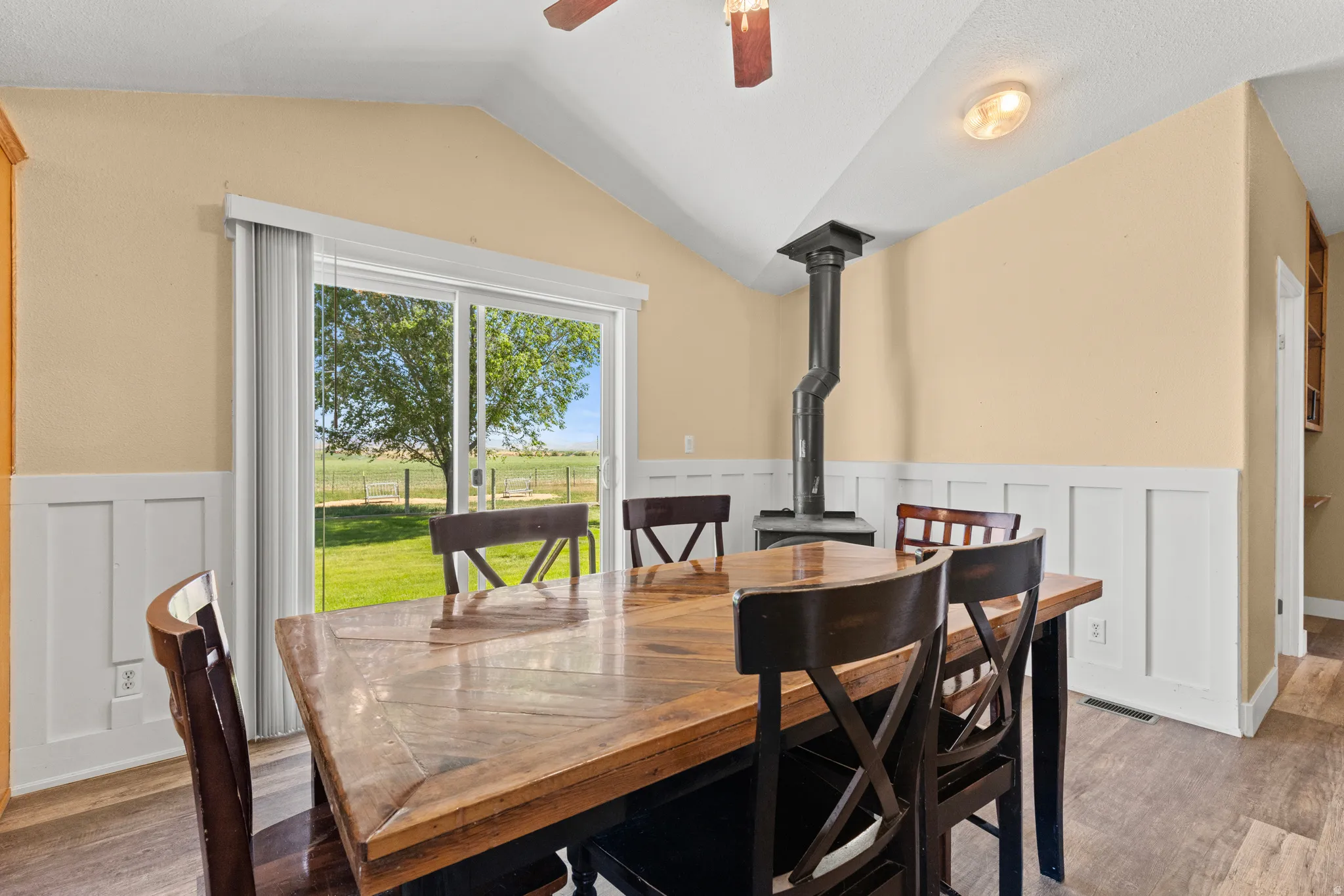 Dining area with sliding glass door access to the exterior, featuring a wood-burning stove, vaulted ceiling, and wainscoting