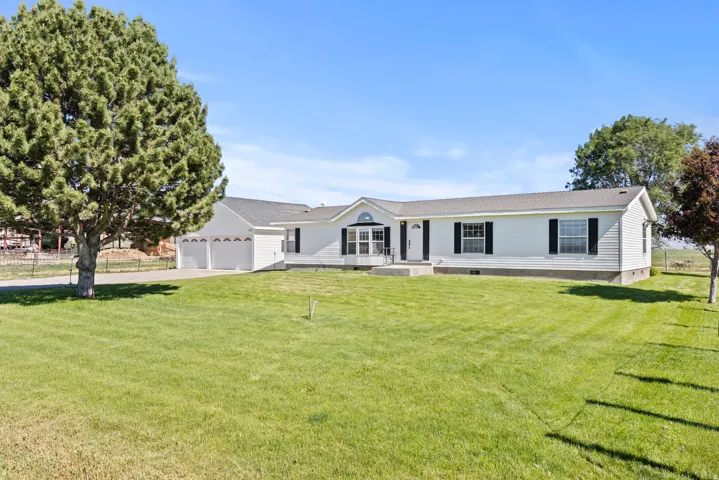White ranch-style residence featuring a three-car garage, mature trees, and a spacious front lawn