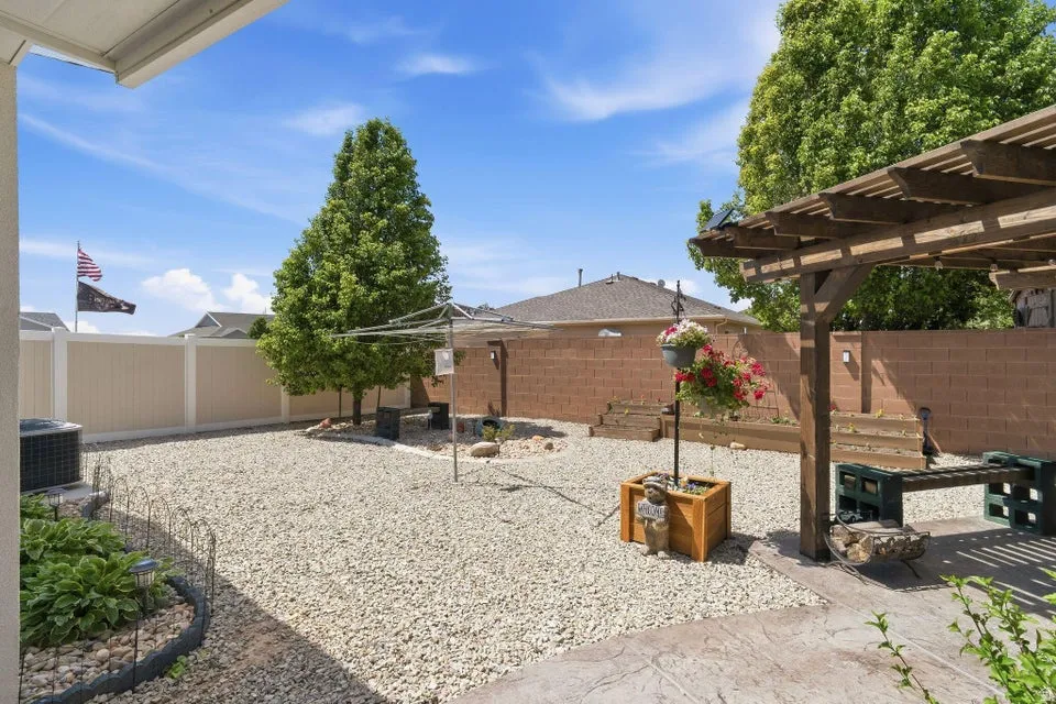 Backyard featuring extensive gravel landscaping, mature trees, a privacy fence, and a wooden pergola