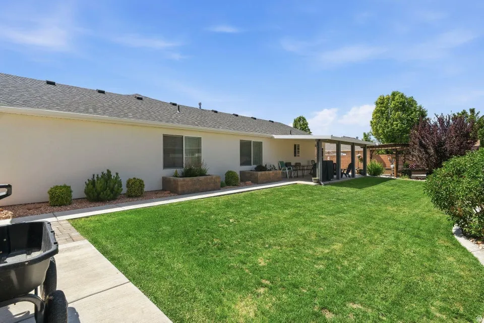 Expansive grassy backyard featuring a covered patio, a separate pergola, and mature landscaping