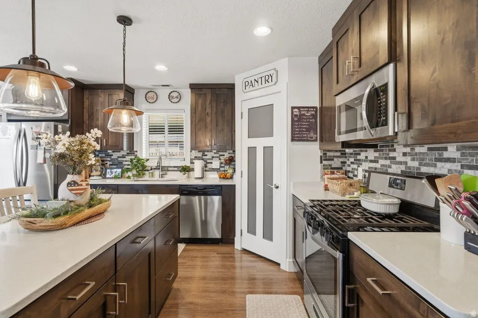 Kitchen featuring wood-finish flooring, dark wood cabinetry with brushed bronze hardware, white countertops, and a mosaic tile backsplash