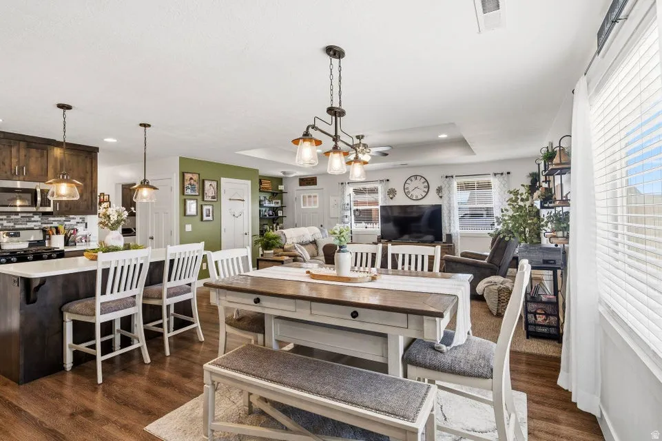 Open-concept living area with wood-finish flooring, a kitchen island featuring a white countertop and pendant lighting, and a dining area with a multi-bulb chandelier