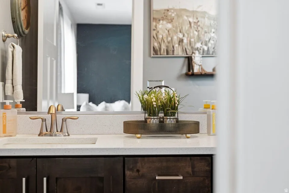 Bathroom vanity featuring a light-toned countertop, dark wood-finish cabinetry with silver-tone pulls, a rectangular undermount sink, and a two-handle faucet in a brushed metal finish